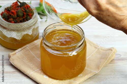 Pouring melted natural beeswax into warm herbal ointment. Woman hand holding a bowl with bee wax. Natural cosmetics from marigold flowers and beeswax.
