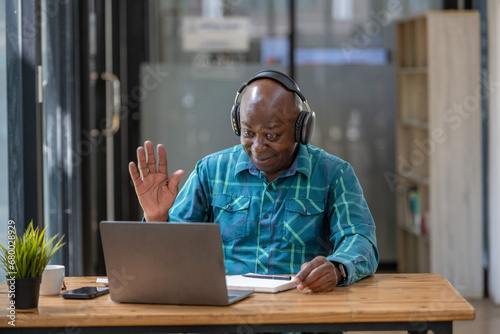 Senior black man wearing headphones waving to people on video call. Long distance greeting.