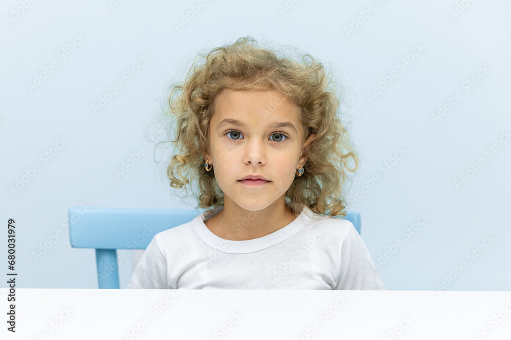 Little girl doing lessons at table on blue background. Education concept learning. Podium or mockup for advertising. Place for text or product on a light blue background Little girl doing lessons at table on blue background. Education concept learning. Podium or mockup for advertising. Place for text or product on a light blue background