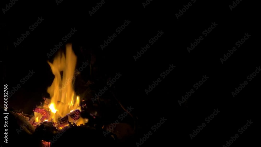 Bonfire on the shore of Lake Issyk-Kul in Kyrgyzstan. Night fire, burning logs, flying sparks. A small torch fire - a small campfire - fire and flames - are highlighted on a black background. 4K