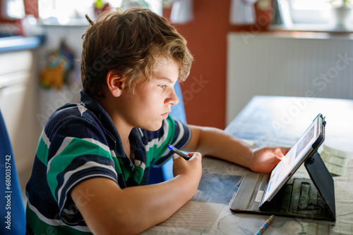 Preteen kid boy learning at home on laptop for school. School child making homework and using notebook and modern gadgets. Home schooling concept. photo