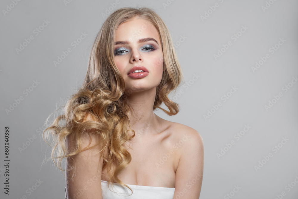 Cute woman with makeup and long healthy blonde shiny wavy hair posing against white studio wall background. Emotional fashion beauty portrait