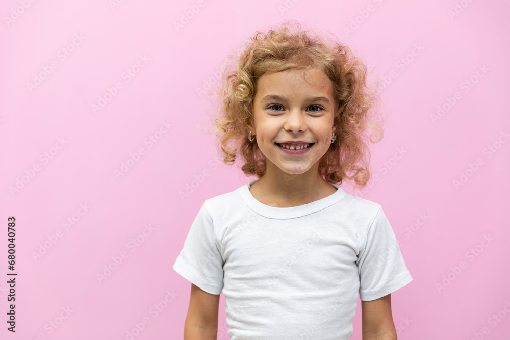Close up head shot portrait with smiling little blonde curly hair girl. Concept happy and beauty kid with good healthy teeth for dental on pink background, six year child looking at camera and posing