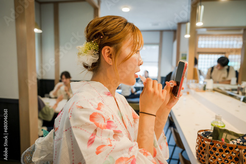 Portrait of a young woman wearing Japanese yukata summer kimono and putting on makeup in a tea shop. Kyoto, Japan. photo