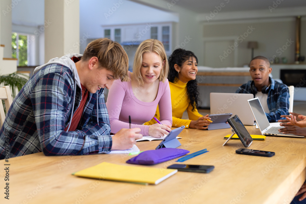 Happy diverse group of teenage friends studying with laptop and tablets at table at home Happy diverse group of teenage friends studying with laptop and tablets at table at home
