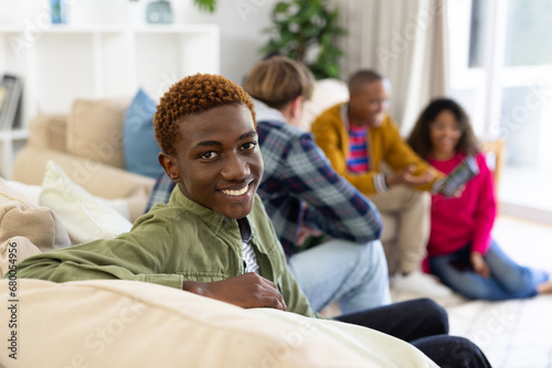 Portrait of happy diverse group of teenage friends using tablet and talking at home photo
