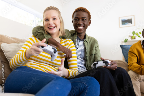 Happy diverse group of teenage friends sitting on couch and playing video games at home photo