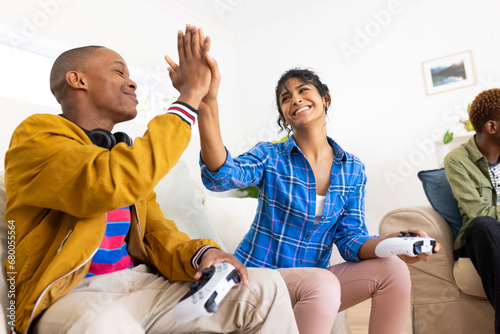 Happy diverse group of teenage friends high fiving and playing video games at home photo