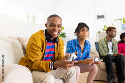 Happy diverse group of teenage friends sitting on couch and playing video games at home photo