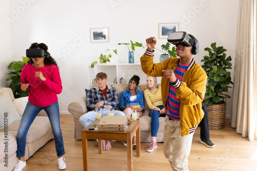 Happy diverse group of teenage friends with pizza using vr headsets and playing at home photo