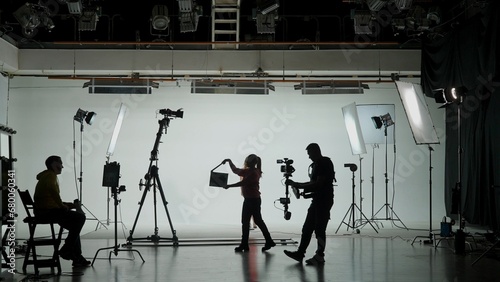 Professional filming pavilion with a white cyclorama. Shooting of a girl in a red dress who sings into a retro microphone. Director, Cameraman and crew in Backstage. photo