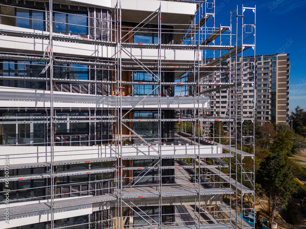 Drone flight along the facade of a modern apartment building under construction surrounded by scaffolding
