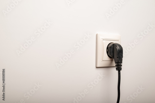 Power socket with inserted plug on white wall, space for text. Electrical supply