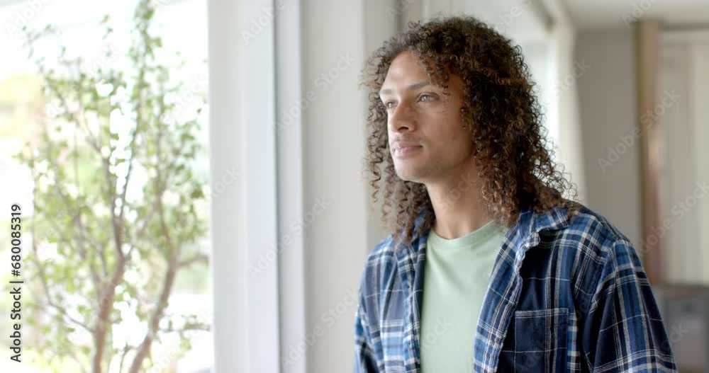 Thoughtful biracial man with long curly hair in sunny living room at home, copy space, slow motion Thoughtful biracial man with long curly hair in sunny living room at home, copy space, slow motion