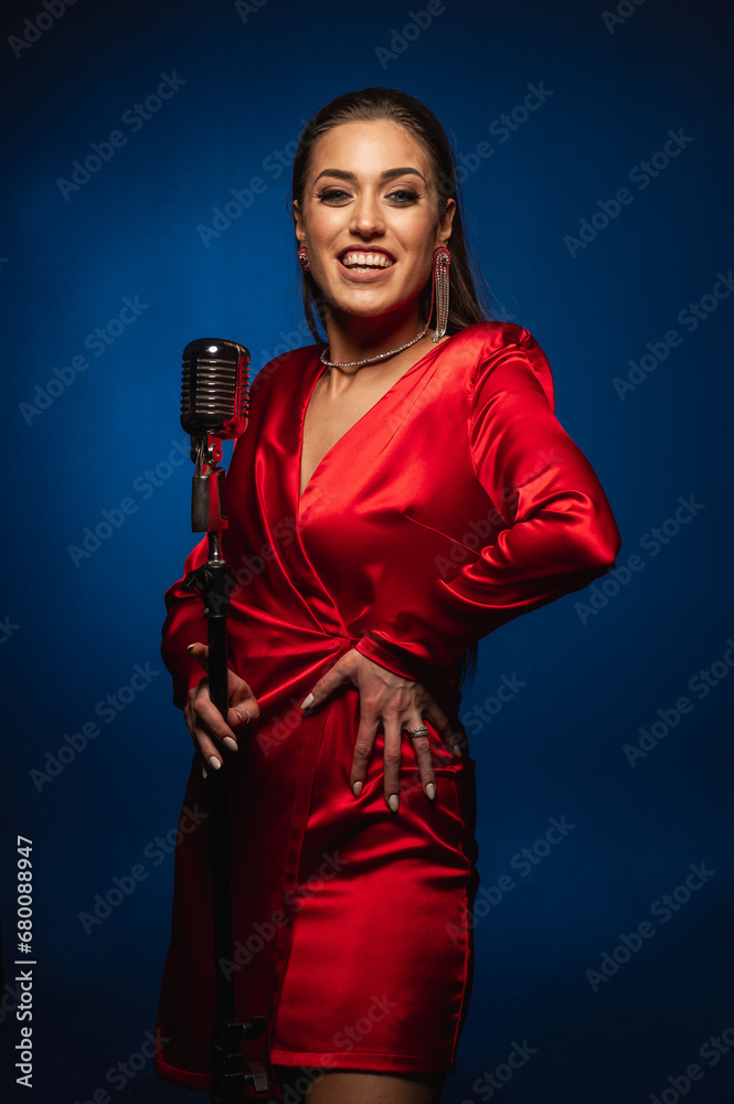 Fototapeta premium A pretty woman in a red dress sings on stage into a retro microphone