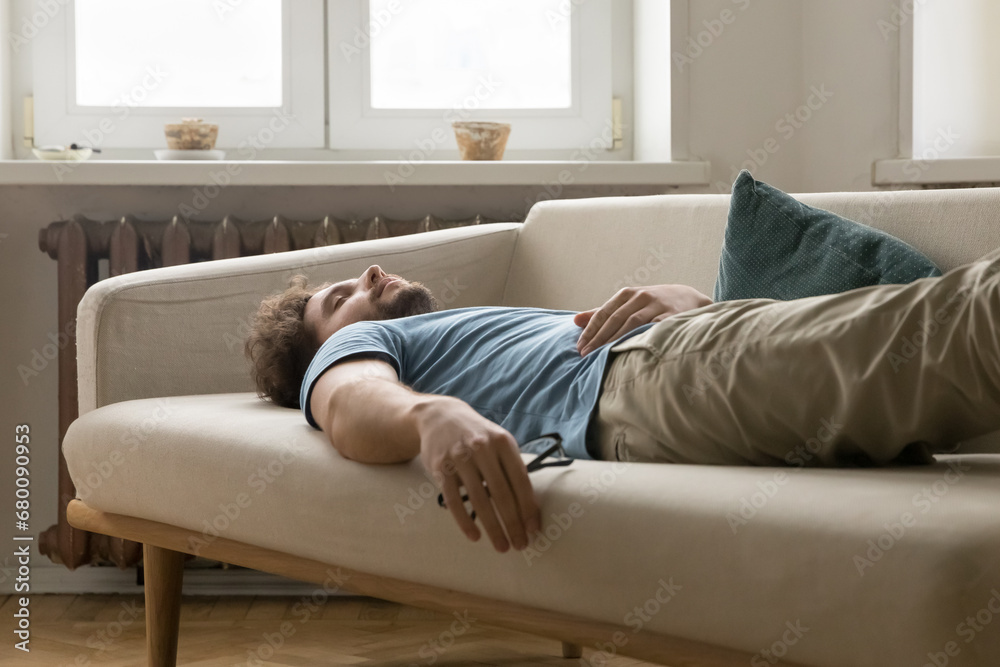 Tired young man having daytime nap on sofa at home. Overloaded guy in casual wear falling asleep on couch in living room, take break, relieving exhaustion after hard working day. Lack of energy, rest Tired young man having daytime nap on sofa at home. Overloaded guy in casual wear falling asleep on couch in living room, take break, relieving exhaustion after hard working day. Lack of energy, rest