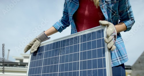 Portrait of happy cauasian woman with gloves holding solar panel in garden, slow motion photo