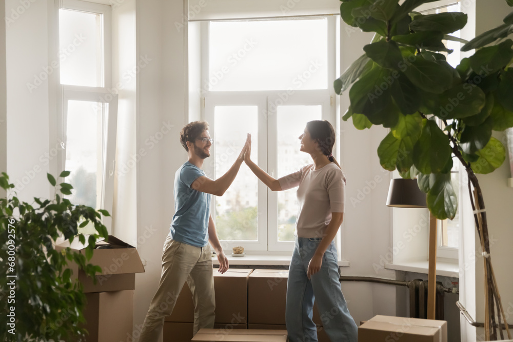 Young couple giving high five congratulate each other with relocation day finish carrying boxes with stuff enjoy move-in at own new house. Bank loan for young family, affordable dwelling, cohabitation - obrazy, fototapety, plakaty 
