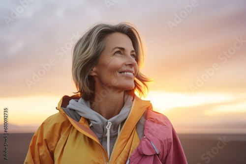 Portrait of a cheerful woman in her 50s wearing a lightweight packable anorak against a vibrant sunset horizon. AI Generation photo