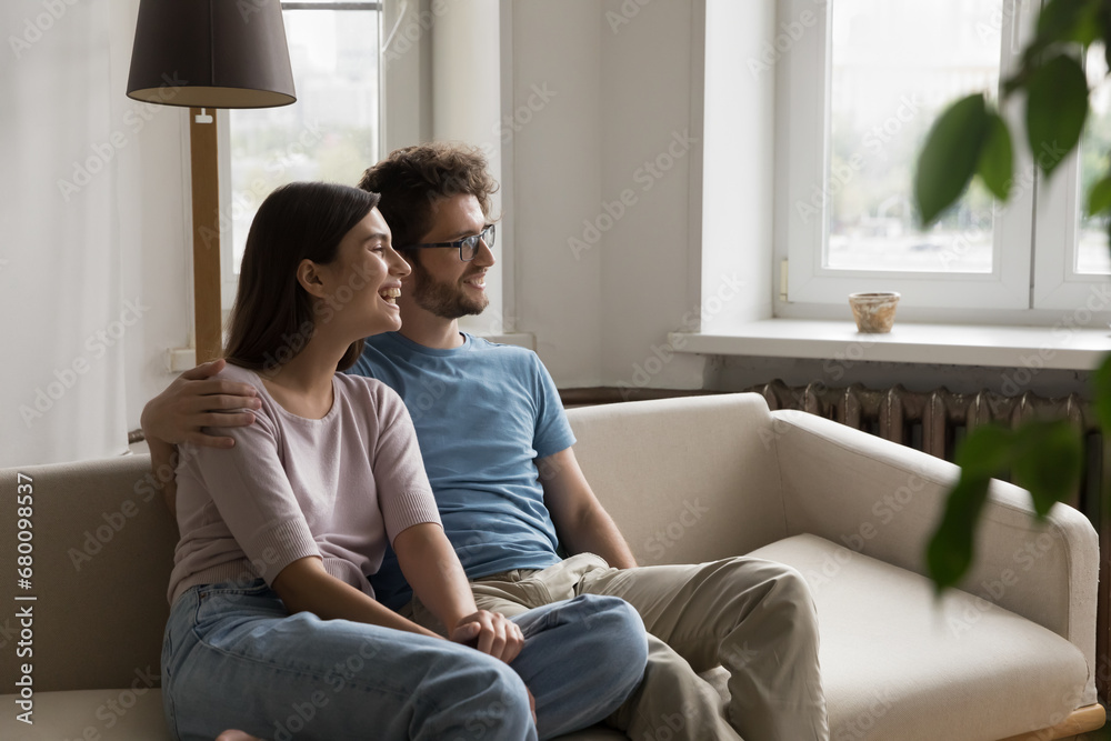 Joyful attractive wife and husband spend time on sofa looking out window, plan bright future, share dreams, laugh, enjoy lazy break, rest on comfortable couch together. Family leisure, weekend relax Joyful attractive wife and husband spend time on sofa looking out window, plan bright future, share dreams, laugh, enjoy lazy break, rest on comfortable couch together. Family leisure, weekend relax