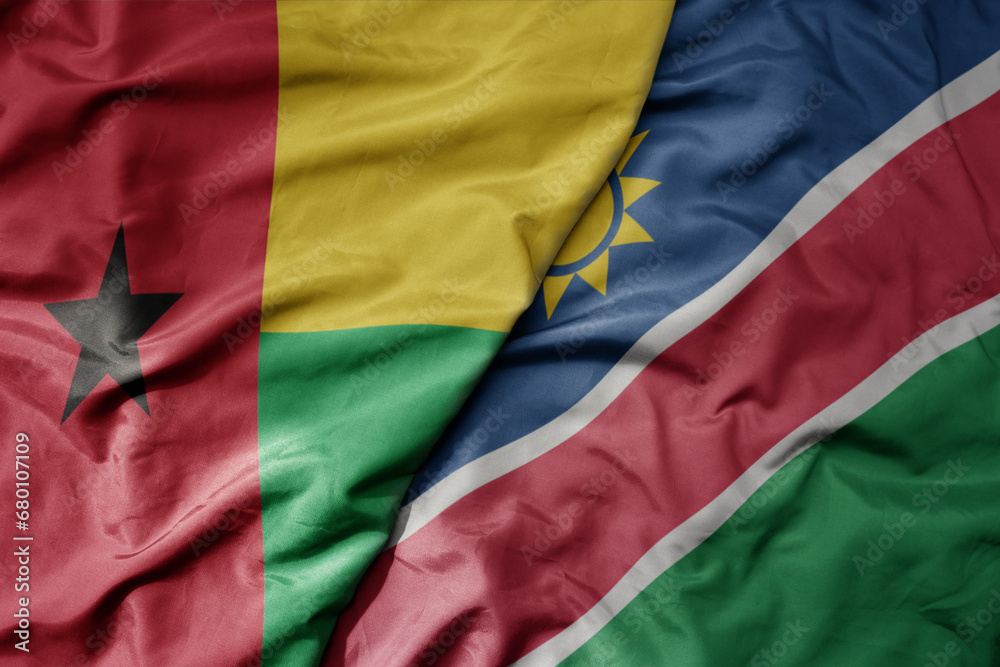 big waving national colorful flag of namibia and national flag of guinea bissau .