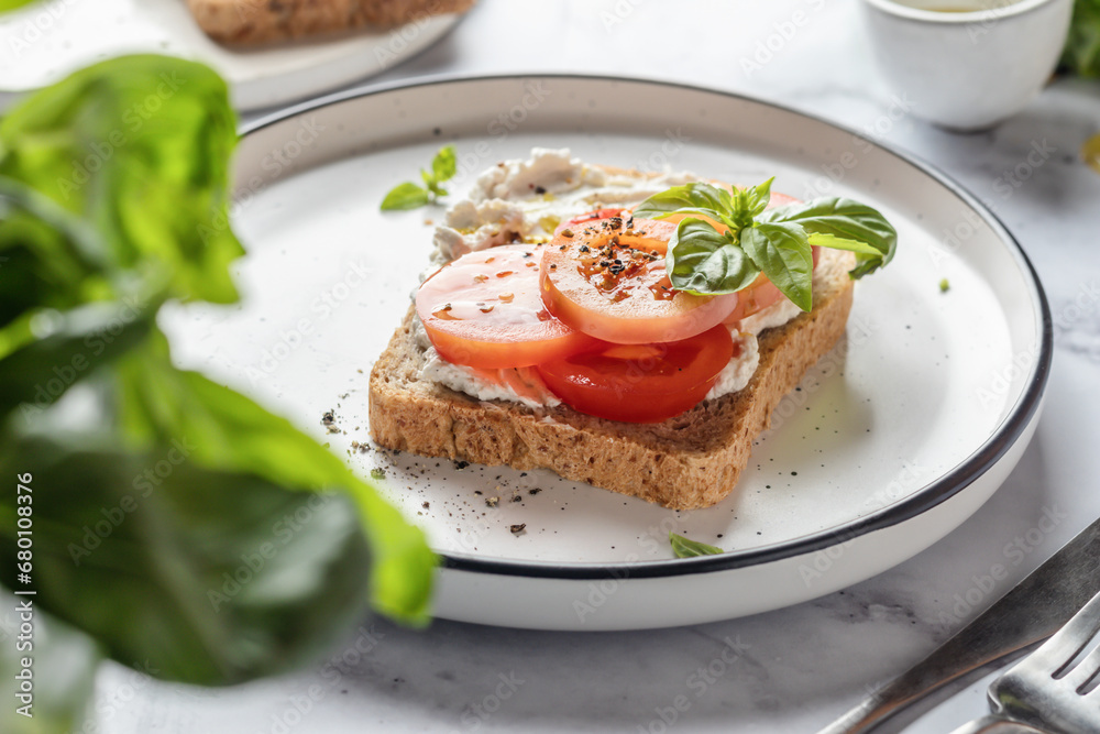 Sandwich or toast with tomatoes, cream cheese, olive oil and basil on a plate on white marble background. Traditional italian mediterranean food Sandwich or toast with tomatoes, cream cheese, olive oil and basil on a plate on white marble background. Traditional italian mediterranean food