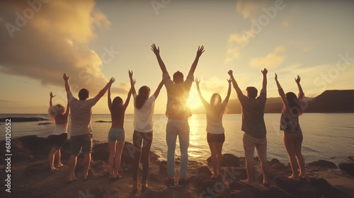 Group of happy friends on the beach, hands raised, sunset light