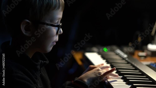 A schoolboy child plays a synthesizer (electric piano or keyboard) at home. Incorrectly plays with one finger. A child's 

interest in music is the first steps. Soft focus.