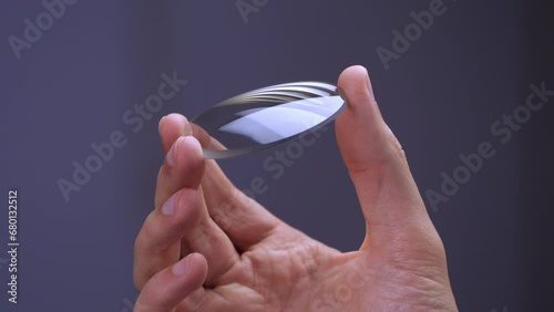 Hand holds a circular glass lens for eyeglasses, modern technology for eyewear quality manufacturing video photo