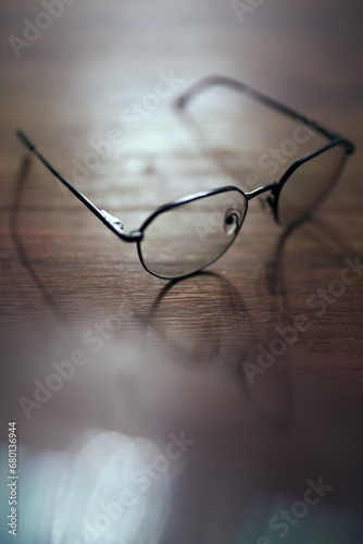 Photo of glasses on wooden table with bokeh and  blurred reflection. Shallow depth of field. Bad eyesight concept image with copy space.
