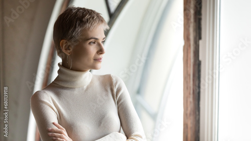 Confident serious business woman looking out of window with arm folded in deep thoughts, thinking of future. Employee, leader, company owner making decision, pondering on work challenge. Head shot