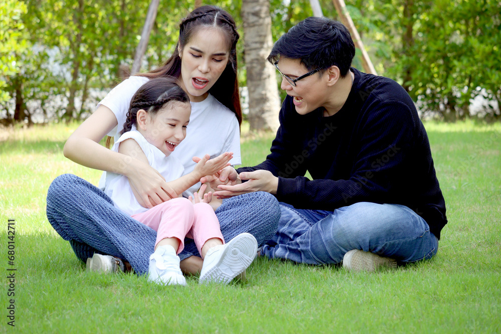 Happy family sitting on green grass, having fun and spending time together in summer garden, cute daughter girl sitting on mother lap during playing with her father at backyard. Family love bonding. Happy family sitting on green grass, having fun and spending time together in summer garden, cute daughter girl sitting on mother lap during playing with her father at backyard. Family love bonding.