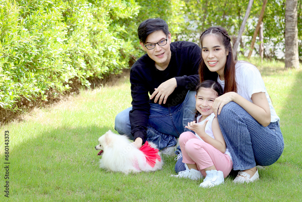 Happy family with pet has fun together in summer green garden. Father, mother and kid play with fluffy white Pomeranian dog, mom hugging cute daughter girl, joyful parents with child at backyard. Happy family with pet has fun together in summer green garden. Father, mother and kid play with fluffy white Pomeranian dog, mom hugging cute daughter girl, joyful parents with child at backyard.