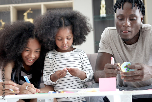 Happy family love bonding  African father and two daughter girls with curly hair enjoy spending time together at home  little child kid and father make hand drawing paper craft card at living room.
