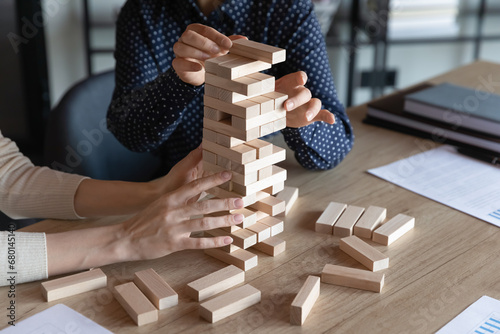 Business team colleagues playing jenga board game together, holding tower building, high stack of wooden blocks from falling, dealing with challenge, risk, teamwork and teambuilding skills. Close up photo