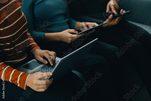 Three beautiful Asian girls using smartphone and laptop, chatting on sofa together at cafe with copy space, modern lifestyle with gadget technology or working woman on casual business concept