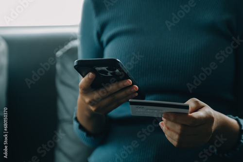 A credit card in the hands of a young businesswoman pays for a business on a mobile phone and on a desk with a laptop.