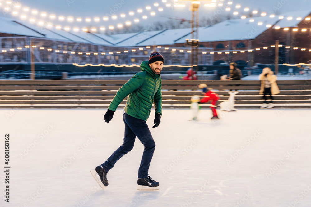 Obraz premium Man ice-skating joyfully in an outdoor rink with festive lights at twilight