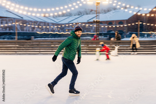 Man ice-skating joyfully in an outdoor rink with festive lights at twilight