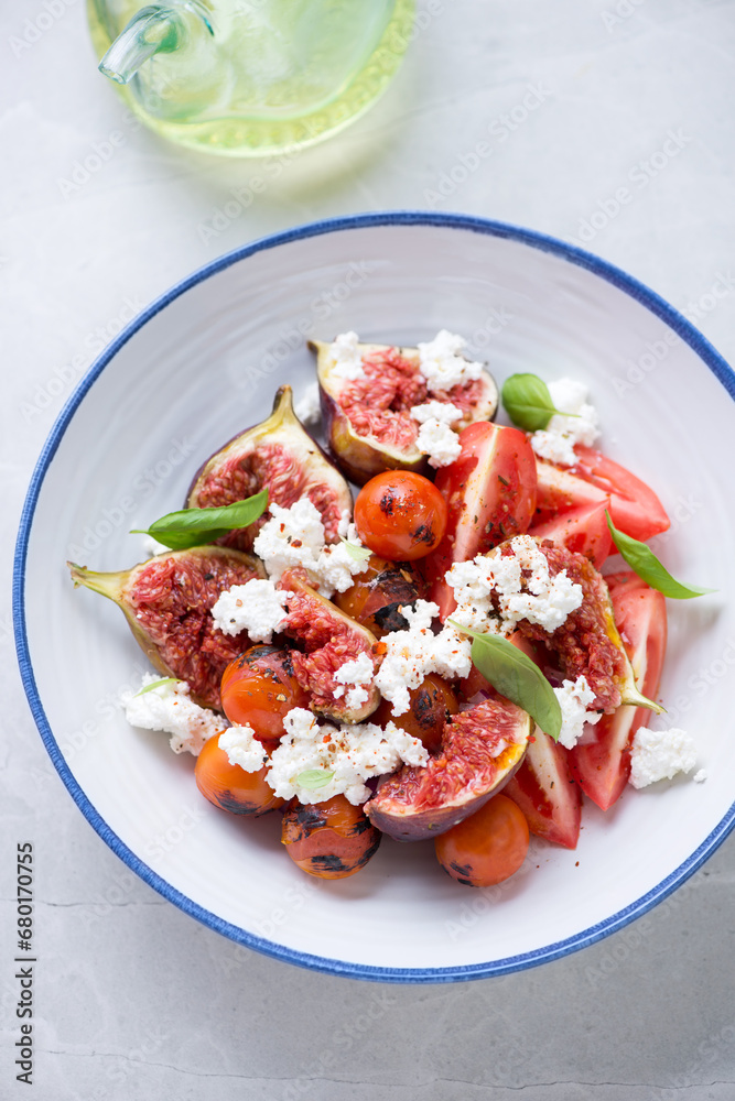 Salad with fresh figs, roasted cherry tomatoes, goat cheese and green basil, vertical shot on a light-grey granite background, elevated view Salad with fresh figs, roasted cherry tomatoes, goat cheese and green basil, vertical shot on a light-grey granite background, elevated view