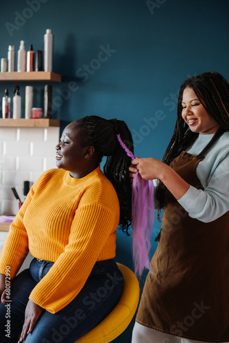 Confident African American hairdresser braiding hair to a smiling female customer in salon