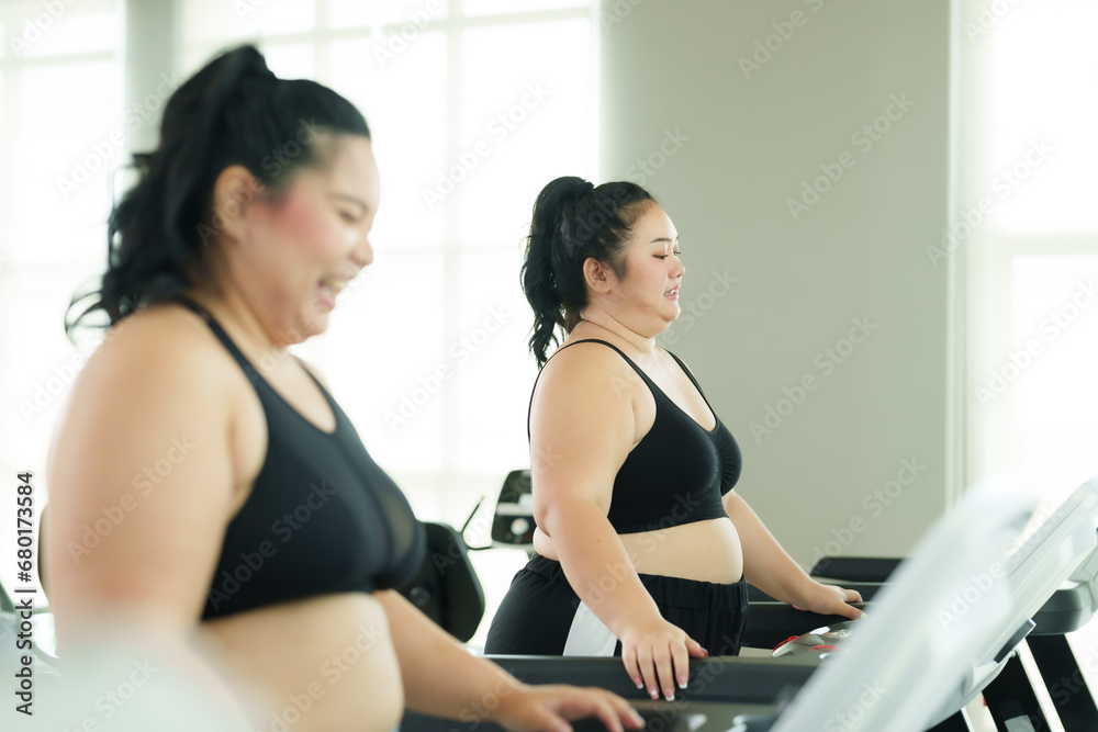 Two plump Asian women friends Invite each other to exercise together in your regular gym. Invite each other to exercise to lose weight. Running on the treadmill in the village fitness center