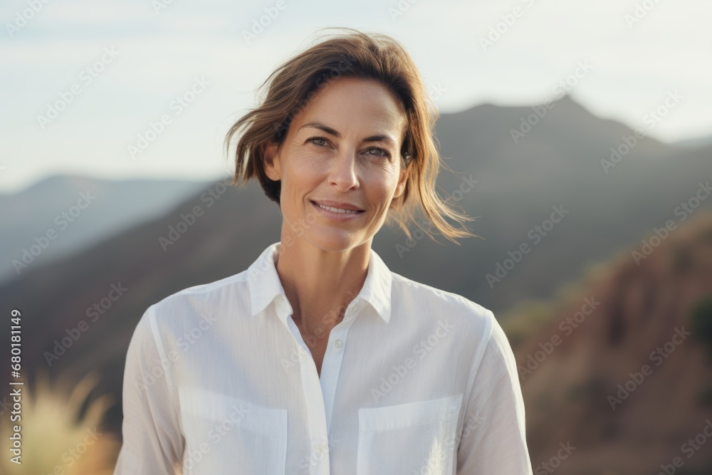 Portrait of a content woman in her 40s wearing a simple cotton shirt against a panoramic mountain vista. AI Generation