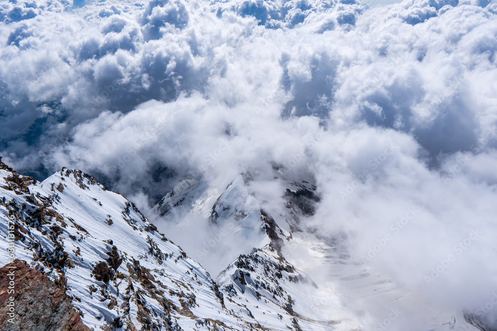 alpine landscape with peaks covered by snow and clouds Cloudy mountains. Mountains in clouds at sunrise in summer. Aerial view of mountain peak with green trees in fog. Top view of mou