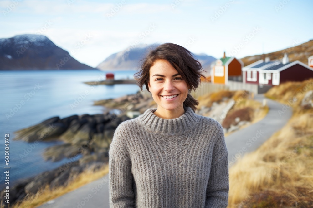 Portrait of a smiling woman in her 30s dressed in a warm wool sweater against a picturesque seaside village. AI Generation