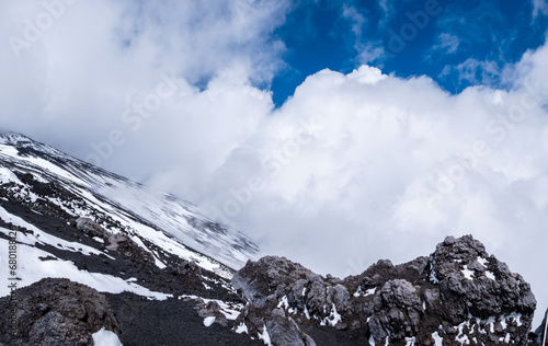 Slope of Mount Etna crater, Sicily island in Italy. Close view of volcanic lava rocks and stones covered with snow in winter. Clouds and smoke from active volcano photo
