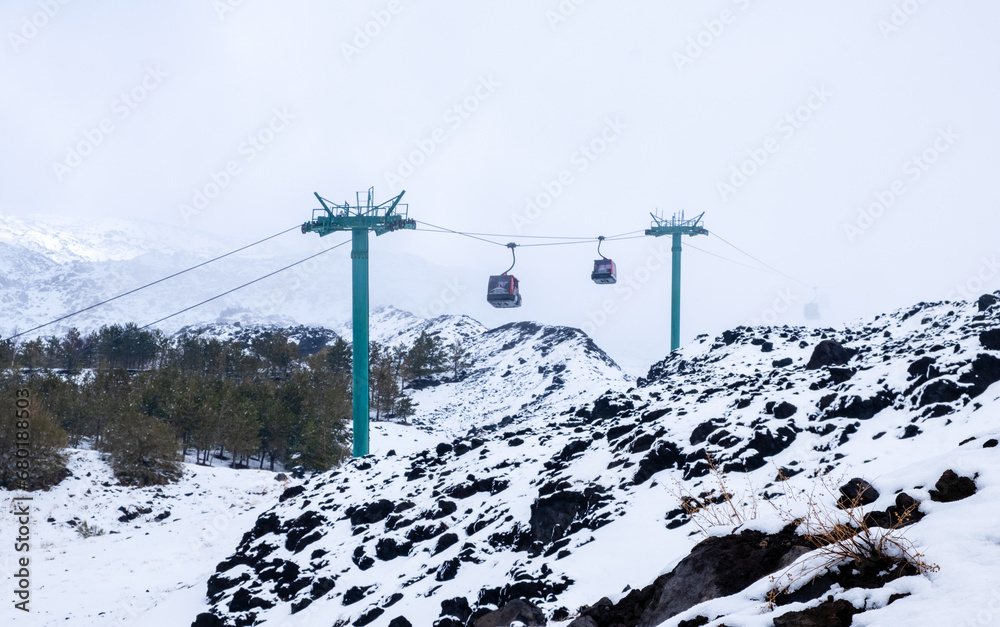 Cable car to Mount Etna national park in winter. View of volcanic terrain with black volcanic lava stones and snow under fog and smoke Cable car to Mount Etna national park in winter. View of volcanic terrain with black volcanic lava stones and snow under fog and smoke