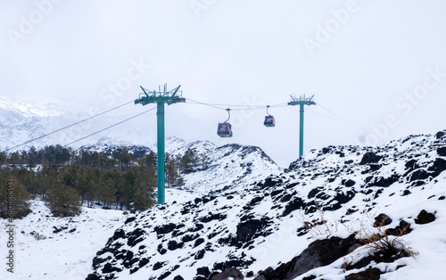 Cable car to Mount Etna national park in winter. View of volcanic terrain with black volcanic lava stones and snow under fog and smoke © Julia Lavrinenko
