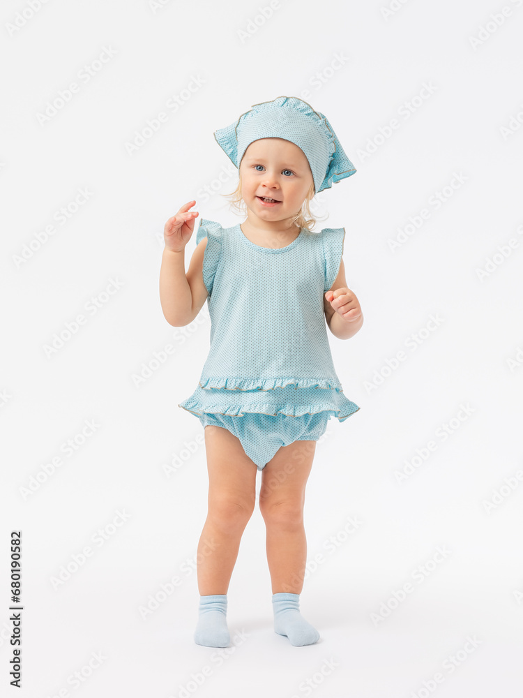 Play, communication, dialogue. A 2-year-old toddler girl stands tall, smiles and looks expressively in a blue dress and socks on a white background. Photo Play, communication, dialogue. A 2-year-old toddler girl stands tall, smiles and looks expressively in a blue dress and socks on a white background. Photo