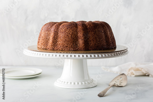 A plain chocolate bundt cake on a pedestal stand against a light background. photo